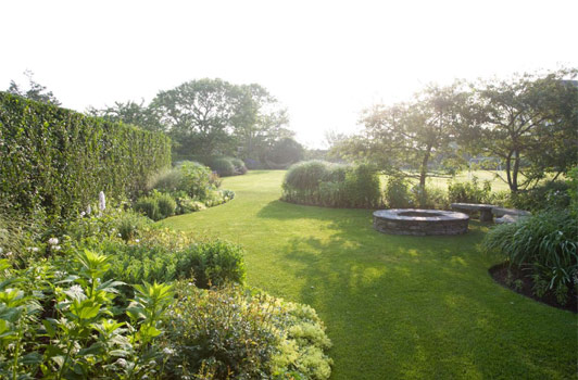 title:A firepit sits quietly behind a grouping of crabapple trees. To the left, an all white garden is featured.