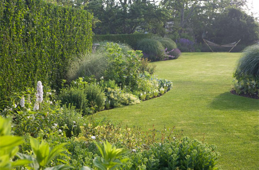 title:A view of the white garden, and the garden beyond featuring a hammock stand.