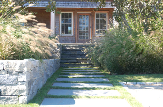 title:A simple walkway lined with native oaks, bayberry, and grasses, lead quietly to the front door.